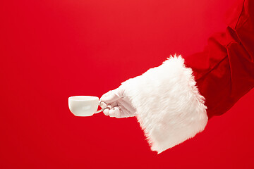 Image showing Christmas coffee. The Santa hand holding cup of cofee isolated on a red background with space for text