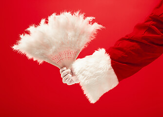 Image showing Hand of Santa Claus holding a toy Christmas retro fan on red background