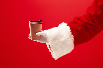 Image showing Christmas coffee. The Santa hand holding cup of cofee isolated on a red background with space for text