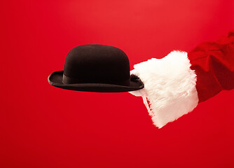 Image showing Hand of Santa Claus holding a male hat on red background