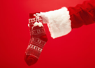 Image showing Hand of Santa Claus holding a Christmas Knitted Socks on red background