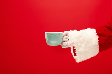 Image showing Christmas coffee. The Santa hand holding cup of cofee isolated on a red background with space for text