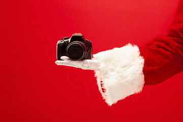 Image showing Hand of Santa Claus holding a camera on red background