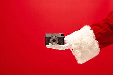 Image showing Hand of Santa Claus holding a camera on red background