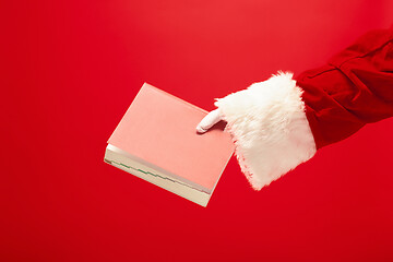 Image showing Hand of Santa Claus holding a notebook on red background