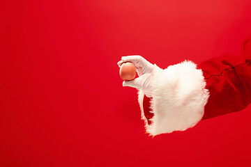 Image showing Hand of Santa Claus holding an egg on red background