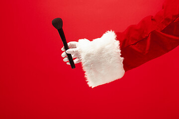 Image showing Hand of Santa Claus holding a makeup brush for powder on red background