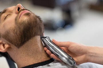 Image showing man and barber with trimmer cutting beard at salon