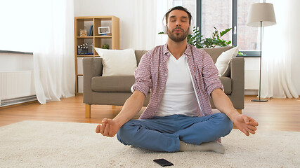 Image showing man in headphones meditating in lotus pose at home