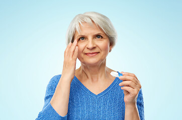 Image showing senior woman applying contact lenses over blue