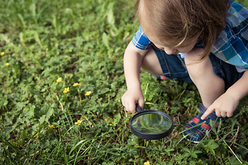 Image showing Happy little boy exploring nature with magnifying glass at the d