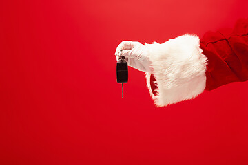 Image showing Hand of Santa Claus holding a gift on red background