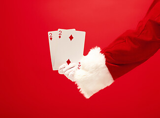 Image showing Hand of Santa Claus holding a playing cards on red background