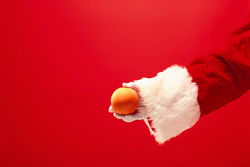 Image showing Hand of Santa Claus holding an orange on red background