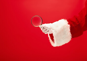 Image showing Hand of Santa Claus holding a magnifier on red background