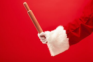 Image showing Hand of Santa Claus holding a culinary rolling pin on red background