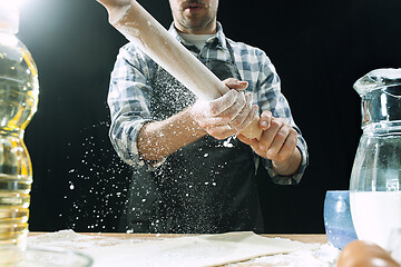 Image showing Professional male cook sprinkles dough with flour, preapares or bakes bread at kitchen table