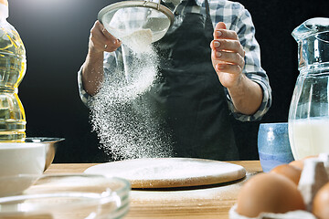 Image showing Professional male cook sprinkles dough with flour, preapares or bakes bread at kitchen table