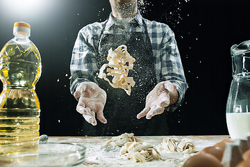 Image showing Professional male cook sprinkles dough with flour, preapares or bakes bread at kitchen table
