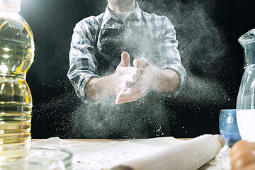 Image showing Professional male cook sprinkles dough with flour, preapares or bakes bread at kitchen table