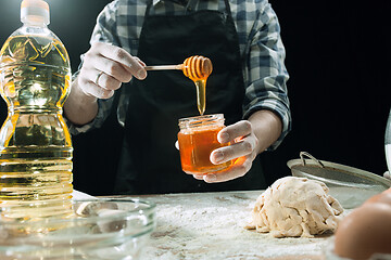 Image showing Professional male cook sprinkles dough with flour, preapares or bakes bread at kitchen table