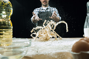 Image showing Professional male cook sprinkles dough with flour, preapares or bakes bread at kitchen table