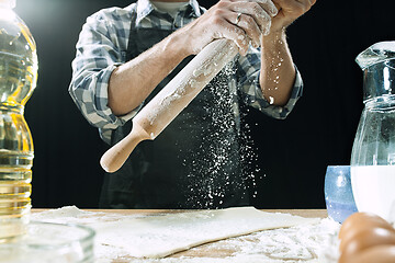 Image showing Professional male cook sprinkles dough with flour, preapares or bakes bread at kitchen table