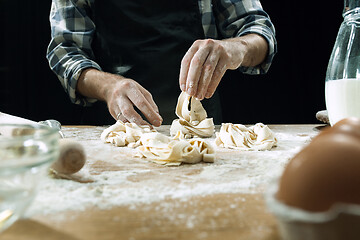 Image showing Professional male cook sprinkles dough with flour, preapares or bakes bread at kitchen table