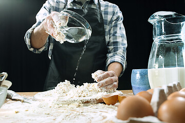 Image showing Professional male cook sprinkles dough with flour, preapares or bakes bread at kitchen table