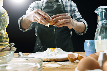 Image showing Professional male cook sprinkles dough with flour, preapares or bakes bread at kitchen table