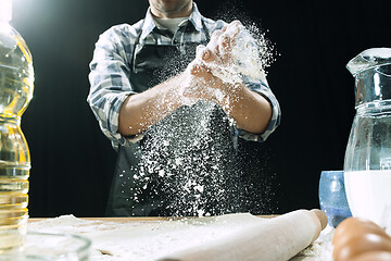 Image showing Professional male cook sprinkles dough with flour, preapares or bakes bread at kitchen table