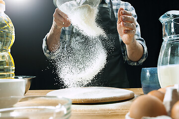 Image showing Professional male cook sprinkles dough with flour, preapares or bakes bread at kitchen table