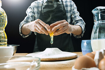 Image showing Professional male cook sprinkles dough with flour, preapares or bakes bread at kitchen table