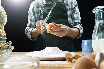 Image showing Professional male cook sprinkles dough with flour, preapares or bakes bread at kitchen table