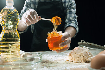 Image showing Professional male cook sprinkles dough with flour, preapares or bakes bread at kitchen table