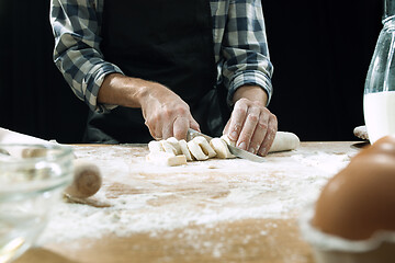 Image showing Professional male cook sprinkles dough with flour, preapares or bakes bread at kitchen table