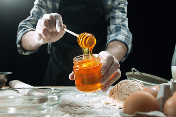 Image showing Professional male cook sprinkles dough with flour, preapares or bakes bread at kitchen table