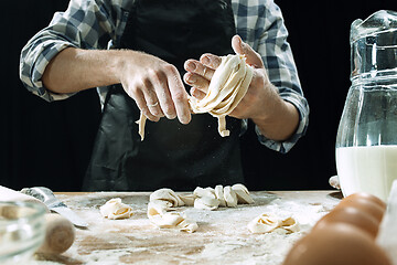 Image showing Professional male cook sprinkles dough with flour, preapares or bakes bread at kitchen table