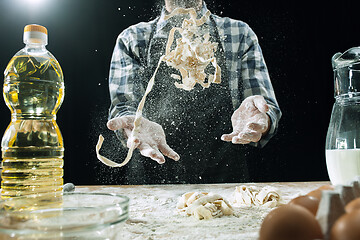 Image showing Professional male cook sprinkles dough with flour, preapares or bakes bread at kitchen table