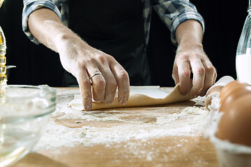 Image showing Professional male cook sprinkles dough with flour, preapares or bakes bread at kitchen table