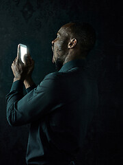 Image showing Studio shot of young serious black African man thinking while talking on mobile phone against black background