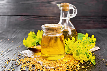 Image showing Oil mustard in jar and decanter with flower on wooden board