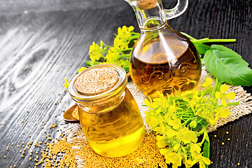 Image showing Oil mustard in jar and decanter with flower on black board