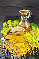 Image showing Oil mustard in jar and decanter with flower on dark wooden board