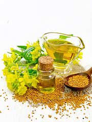 Image showing Oil mustard in jars and gravy boat on wooden board