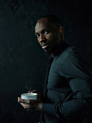 Image showing Stylish young black man with cup of coffee posing on dark background.