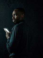 Image showing Studio shot of young serious black African man thinking while talking on mobile phone against black background