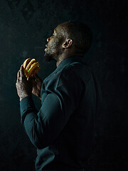 Image showing young african american man eating hamburger and looking away on black studio