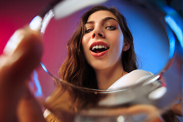 Image showing The surprised young woman in party clothes posing with glass of wine.