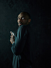Image showing Studio shot of young serious black African man thinking while talking on mobile phone against black background